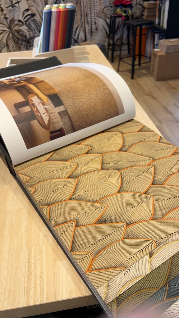 Échantillon de papier peint avec des motifs géométriques en relief et des teintes naturelles, présenté dans le showroom Axirénov.