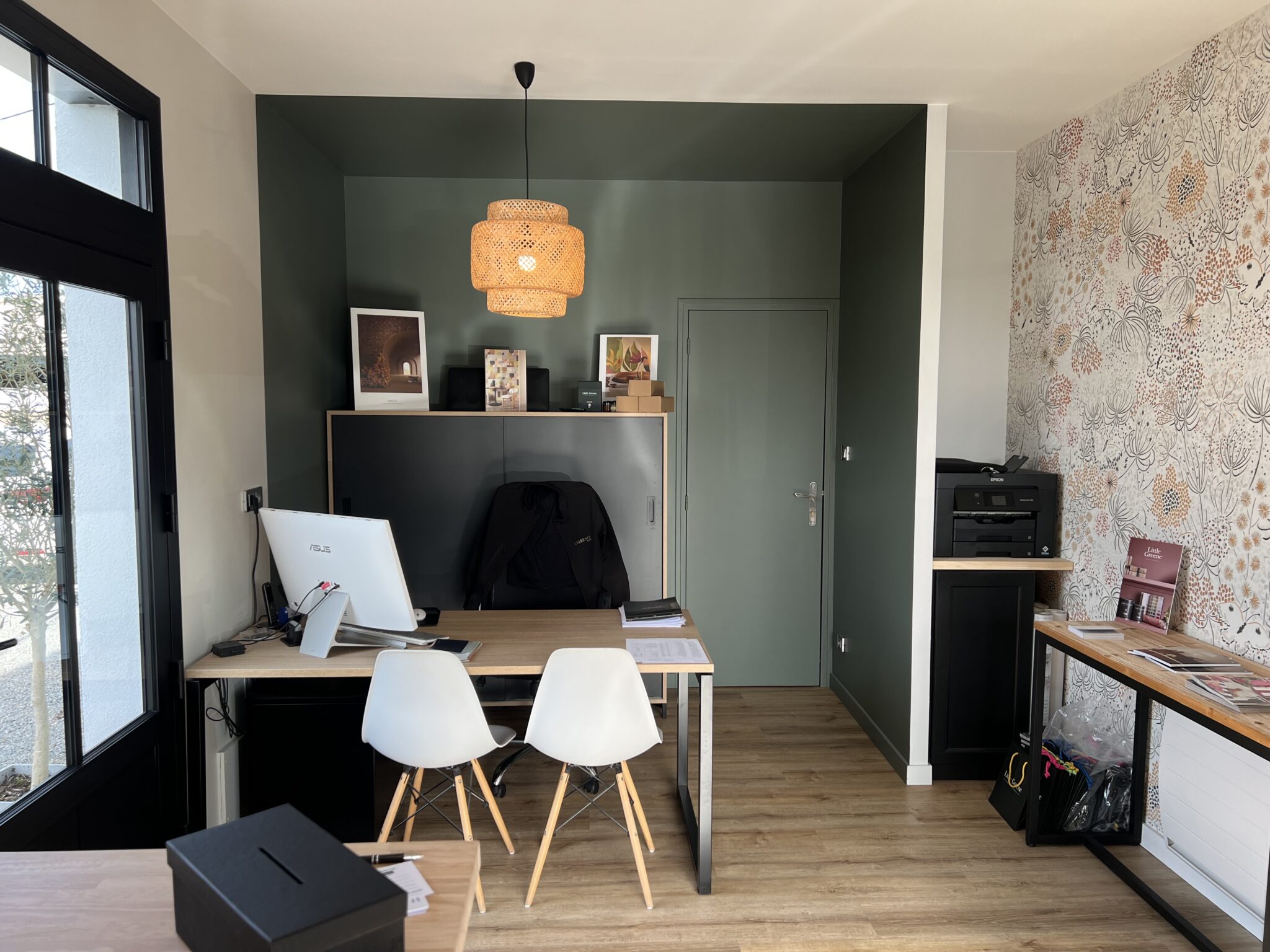 Bureau d'Axirénov Treillières avec un mur peint en vert foncé, du papier peint floral, un bureau en bois clair et une suspension en rotin.