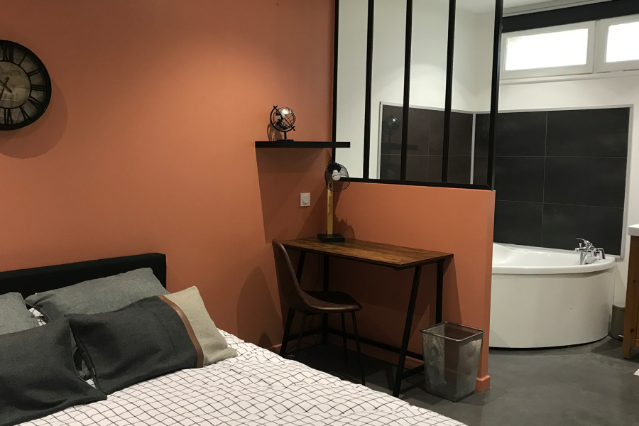 Chambre en colocation à Nantes avec mur terracotta, verrière noire, coin bureau en bois et salle de bain attenante moderne. Axirenov