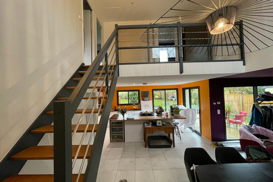 Maison moderne à Orvault avec escalier métallique et bois, mezzanine ouverte, et murs peints dans des teintes chaleureuses orange et prune. Axirenov