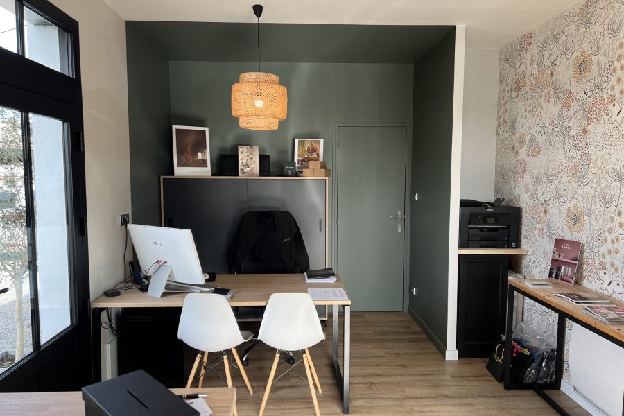 Bureau d'Axirénov Treillières avec un mur peint en vert foncé, du papier peint floral, un bureau en bois clair et une suspension en rotin.